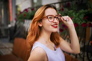 A woman with red hair and glasses is smiling and posing for a photo in a park
