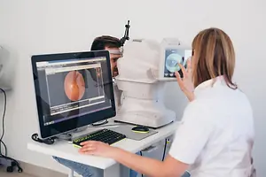 Optometrist examining a patient with a digital eye imaging device and retinal scan displayed on a monitor