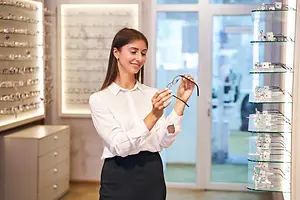 Optical shop employee holding and inspecting eyeglass frames