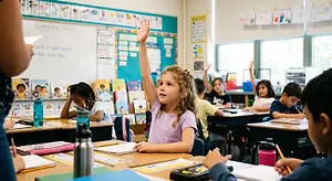 Elementary school students seated at desks during a classroom lesson, with one girl raising her hand