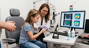 Optometrist examining a young girl's eye in a clinical exam room