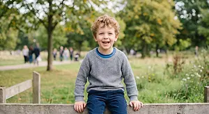 Smiling young boy sitting on a wooden fence in a park