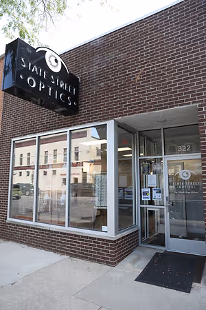 The exterior of the State Street Optics store with a sign displaying the words State Street Optics on top and a number 322 on the glass door