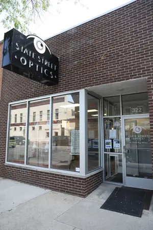 The exterior of the State Street Optics store with a sign displaying the words State Street Optics on top and a number 322 on the glass door