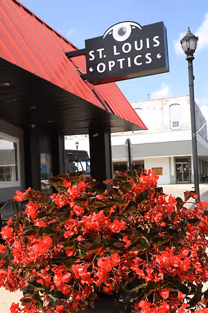 A red building with a sign that says St. Louis Optics and a red flower plant in front of it.