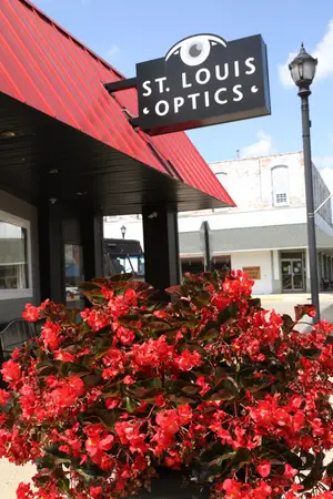 A red building with a sign that says St. Louis Optics and a red flower plant in front of it.
