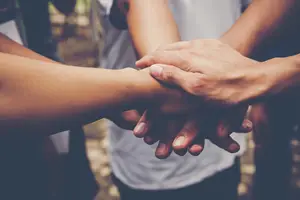 Five hands from different people are stacked on top of each other, indicating unity and teamwork.