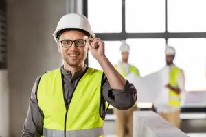 A man in a safety vest and helmet is standing in a construction site