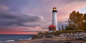 A lighthouse with a red roof and a white tower standing on a rocky shore with a cloudy sky in the background