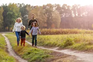 A man, woman, and two kids are running together in a field with trees in the background