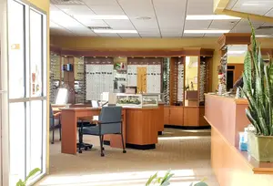 Inside of an optical shop with wooden counters, a desk, and a potted plant.