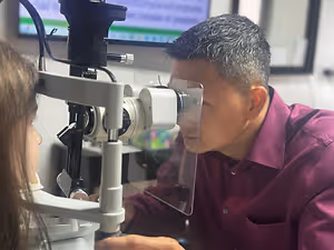 An optometrist is examining a young girl's eyes with an ophthalmoscope in an eye clinic.