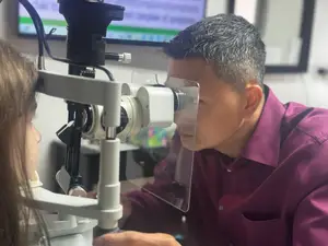 An optometrist is examining a young girl's eyes with an ophthalmoscope in an eye clinic.