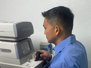 A man in a blue shirt is standing in front of an eye test machine and holding a black handle on it.