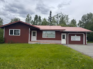 A red building with white doors and windows is on a grassy field under a cloudy sky