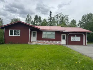 A red building with white doors and windows is on a grassy field under a cloudy sky