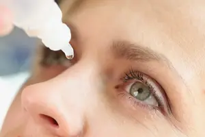 A closeup of a woman's face while she applies eye drops
