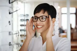 A woman is smiling and holding her glasses in an optician's shop.