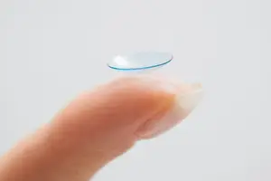 A person's finger holding a contact lens on a white background