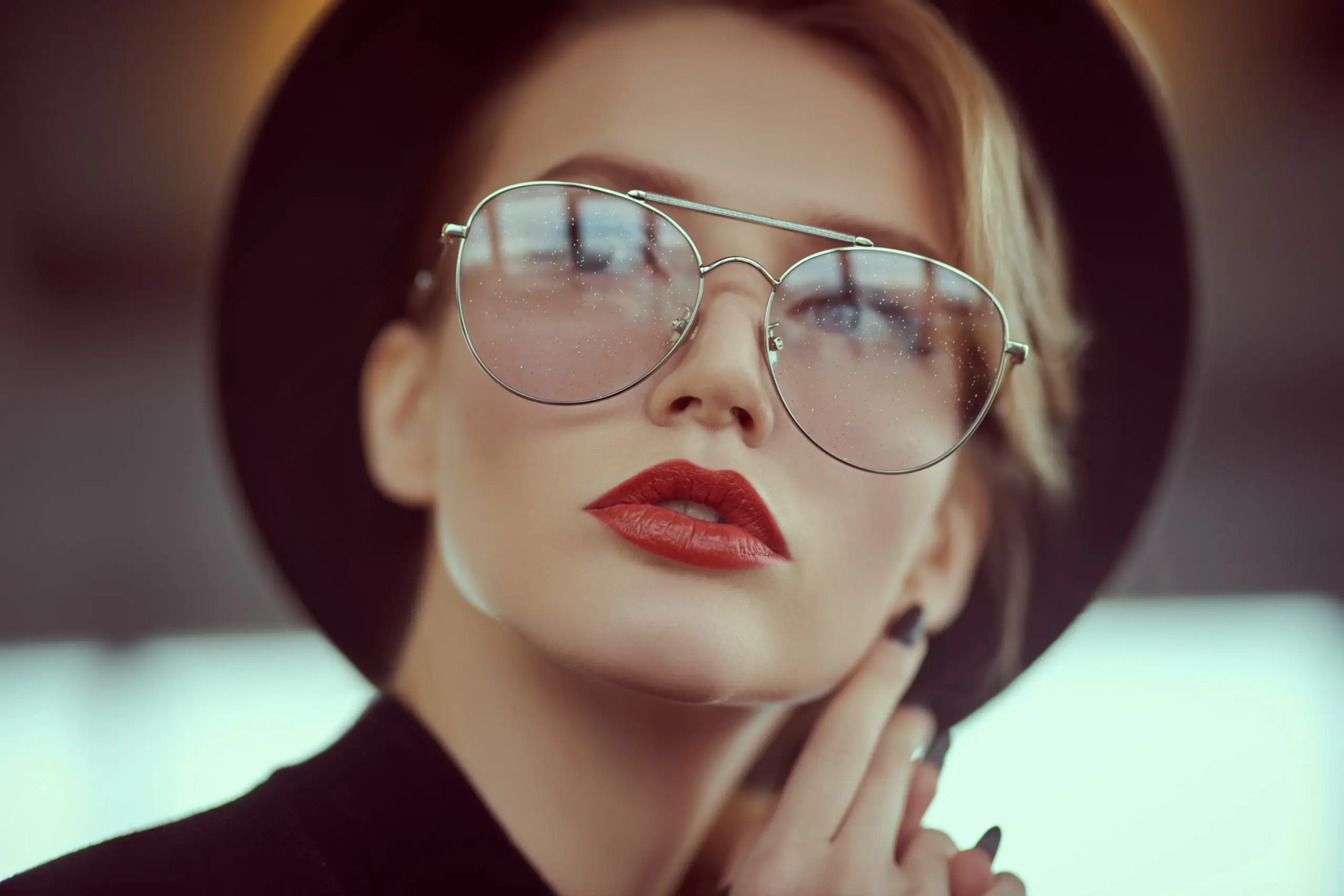 Woman with red lipstick wearing sunglasses and a black hat posing for a photo