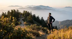 A runner stands on a trail with mountains and a sunrise in the background.