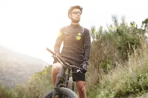 A man stands on a bicycle with a mountain in the background