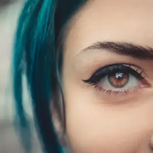Close up of a woman's face with brown eyes and teal hair looking straight ahead