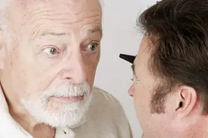 An old man is looking at another man who is holding a black object in front of his eye.