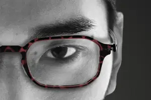 A close up of a person's eye wearing red and black glasses with a blurred background