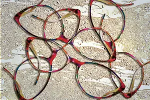 A close-up of several colorful glasses frames scattered on a sandy surface, possibly a beach.