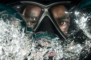 A closeup of a person wearing a scuba diving mask with water droplets on it