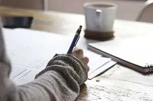 Person writing on paper with a pen on a wooden table.