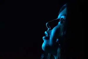 woman with long black hair looking upward in a dark room with blue light