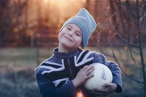 A smiling boy in a hat holding a soccer ball outdoors