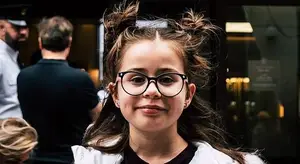 Girl with glasses and a ponytail smiling at the camera