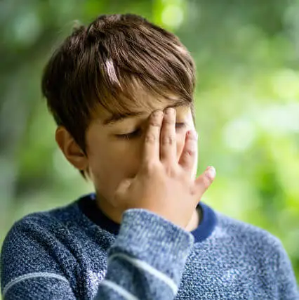 Boy covering his face with his hand in a forest
