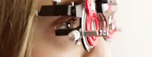 A young woman wearing glasses with a red-lensed device on her head, possibly for an eye examination