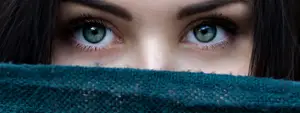 Close up of a woman with dark hair and green eyes peeking through a knitted green fabric.