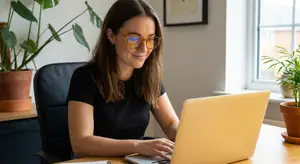 Woman sitting at a desk wearing glasses and typing on a laptop.