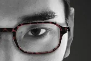 Black and white close up of a person wearing glasses with red patterns on the frame