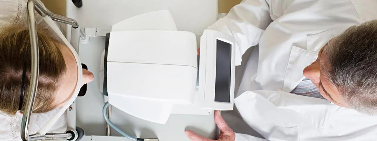 An eye doctor is showing a patient how to use an eye exam machine.
