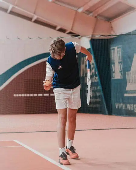 A boy with a tennis racket and ball in a tennis court
