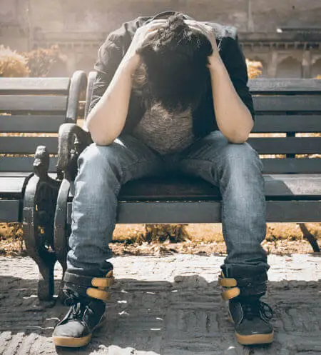 A person sitting on a bench with his head in his hands