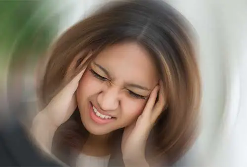 Woman holding her head in pain and smiling with a blurry background