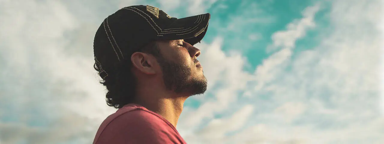 A man with a hat and beard looking up at the sky with clouds