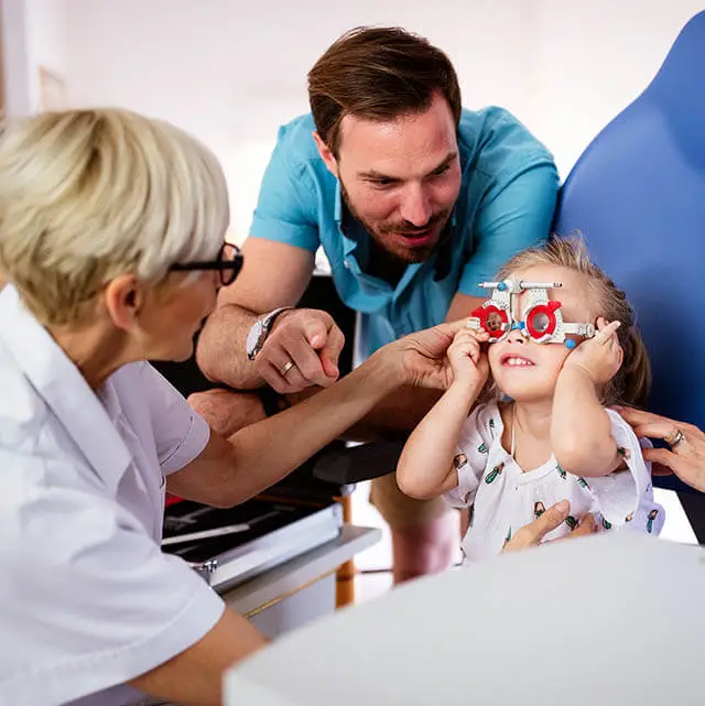 A family with a young girl at an optometrist's office where the child is having her eyes examined by a doctor and her parents are present.