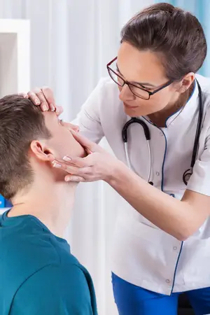 A female doctor wearing a white lab coat and glasses is examining a patient's ear.