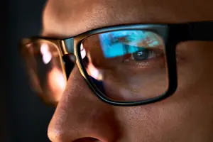 Close-up of a man wearing glasses looking at a computer screen with reflections on the glasses