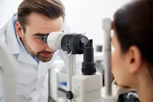 A male optometrist examining a female patient's eye with a microscope