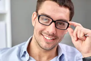 A man with glasses adjusting them and smiling at the camera